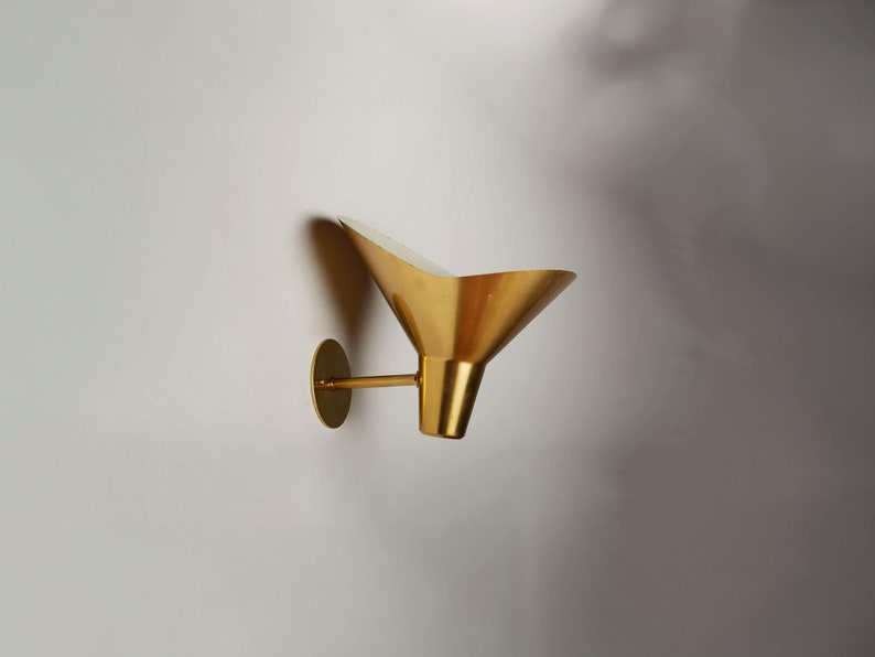 May include: A gold-toned wall sconce with a funnel-shaped shade. The sconce has a circular base and a single arm that extends to the shade.