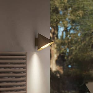 Puede incluir: Un aplique de pared exterior marrón con una pantalla en forma de cono. La luz está montada en una pared blanca y proyecta un haz de luz.