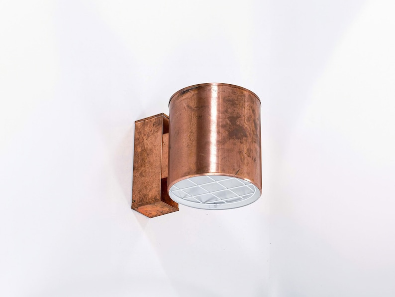 May include: A copper wall sconce with a cylindrical shade and a rectangular base. The shade has a white grid pattern on the inside.