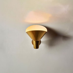 May include: A gold wall sconce with a white frosted glass shade. The sconce is mounted on a white wall.