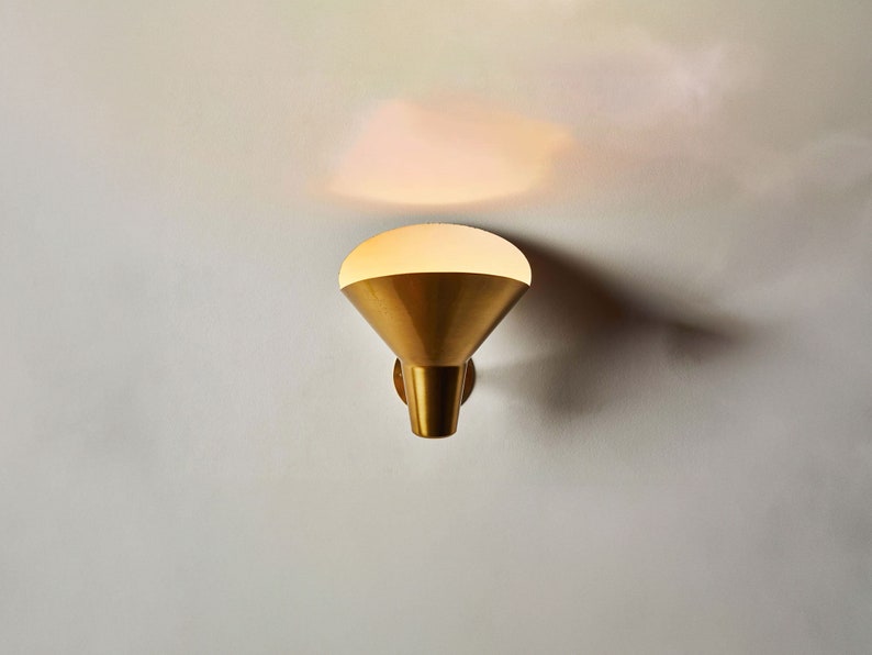 May include: A gold wall sconce with a white frosted glass shade. The sconce is mounted on a white wall.