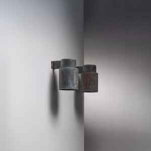 May include: Two copper wall sconces with a weathered finish. The sconces are mounted on a white wall.