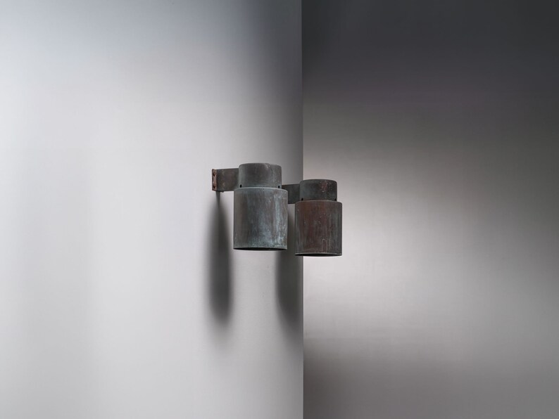 May include: Two copper wall sconces with a weathered finish. The sconces are mounted on a white wall.