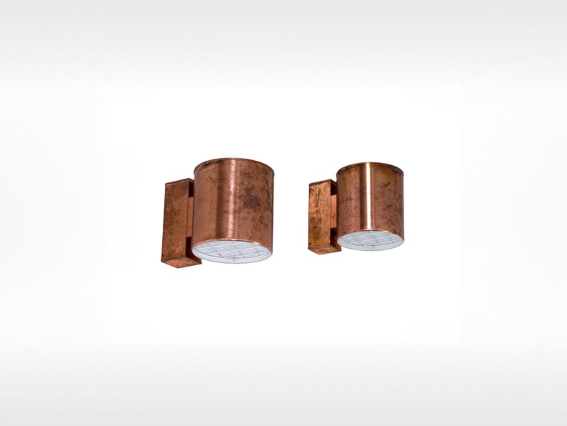 May include: Two copper wall sconces with a white light source. The sconces are cylindrical in shape and have a distressed finish.