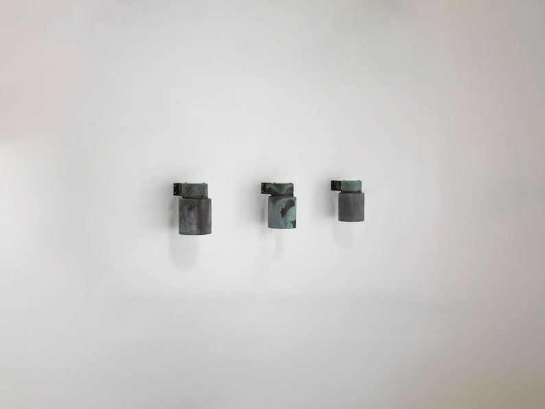 May include: Three wall-mounted lights with a weathered copper finish. The lights are cylindrical in shape and have a slightly angled design.