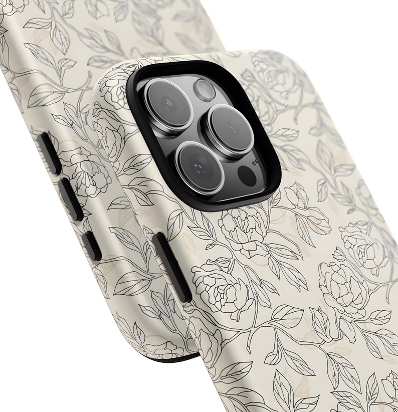 May include: Close-up of a phone case with a floral design. The case is off-white with a black outline of flowers and leaves. The camera lenses are visible, with a black border.