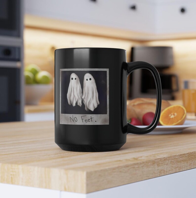 May include: Black coffee mug with a white ghost image and the text "No Feet." printed on it.