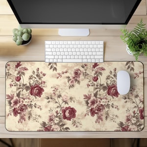 May include: A floral mouse pad with a cream background and a pattern of burgundy and pink roses. A white mouse and keyboard are on the desk. A computer monitor and small potted plants are also visible.