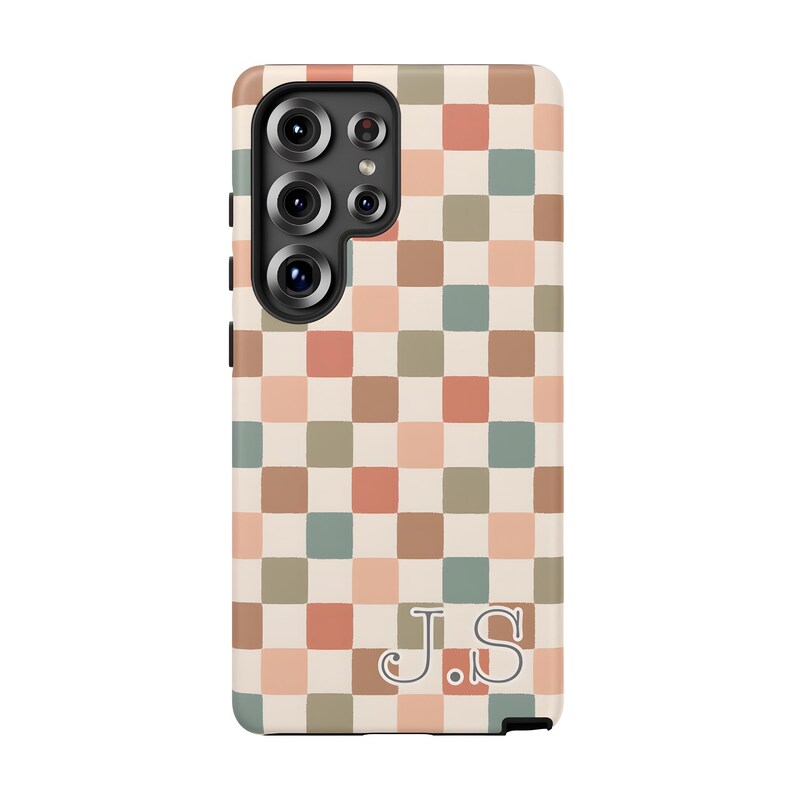 May include: A phone case with a checkerboard pattern in shades of beige, peach, green, and brown. The case has a camera cutout and the initials "J.S." in a cursive font at the bottom.