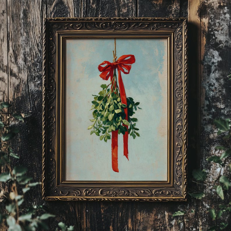 May include: A framed print featuring a sprig of mistletoe tied with a red ribbon and bow. The artwork has a light blue background and is set in an ornate, dark gold frame. The image is against a dark wood background.