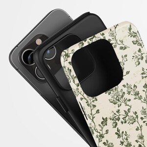 Puede incluir: Tres fundas de tel&eacute;fono apiladas, que muestran un dise&ntilde;o floral. La funda superior presenta un fondo crema con patrones florales verdes. La funda del medio es negra y la funda inferior es un tel&eacute;fono gris. Las fundas est&aacute;n en &aacute;ngulo, revelando la c&aacute;mara del tel&eacute;fono.