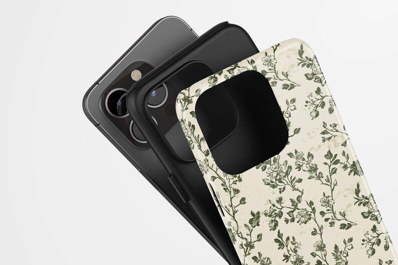 Puede incluir: Tres fundas de tel&eacute;fono apiladas, que muestran un dise&ntilde;o floral. La funda superior presenta un fondo crema con patrones florales verdes. La funda del medio es negra y la funda inferior es un tel&eacute;fono gris. Las fundas est&aacute;n en &aacute;ngulo, revelando la c&aacute;mara del tel&eacute;fono.