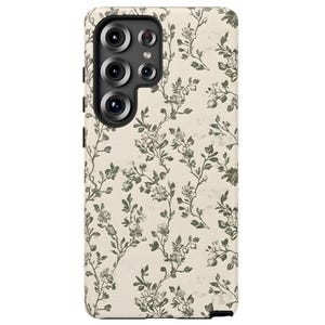 Puede incluir: Una funda de tel&eacute;fono con un estampado floral. La funda es de color beige claro con un dise&ntilde;o repetido de ramas florales verdes. Las lentes de la c&aacute;mara son visibles en la parte superior izquierda.