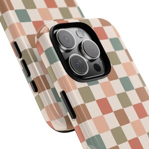 May include: A phone case with a retro checkerboard pattern in shades of beige, peach, green, and brown. The case has a black camera lens surround and black buttons on the side. The phone case is designed to protect the phone.