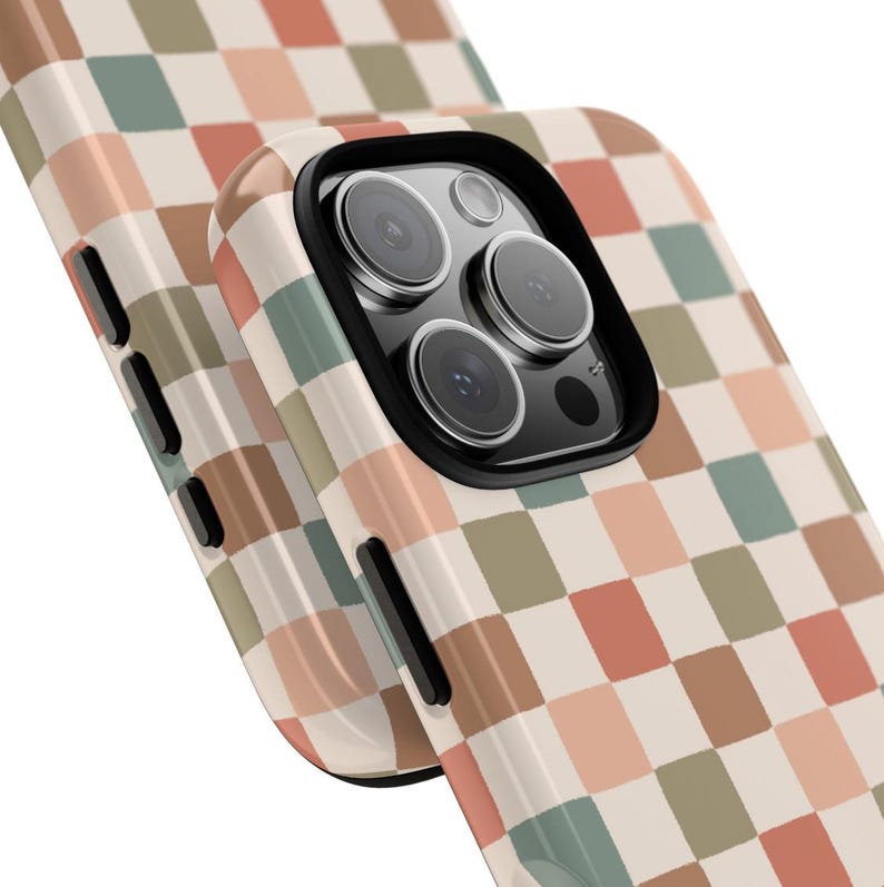 May include: A phone case with a retro checkerboard pattern in shades of beige, peach, green, and brown. The case has a black camera lens surround and black buttons on the side. The phone case is designed to protect the phone.