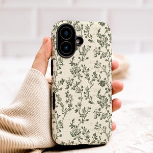 Puede incluir: Una funda de tel&eacute;fono con un estampado floral. La funda presenta un fondo color crema con un dise&ntilde;o repetido de vides y flores florales verdes. La funda del tel&eacute;fono tiene un recorte para la c&aacute;mara.
