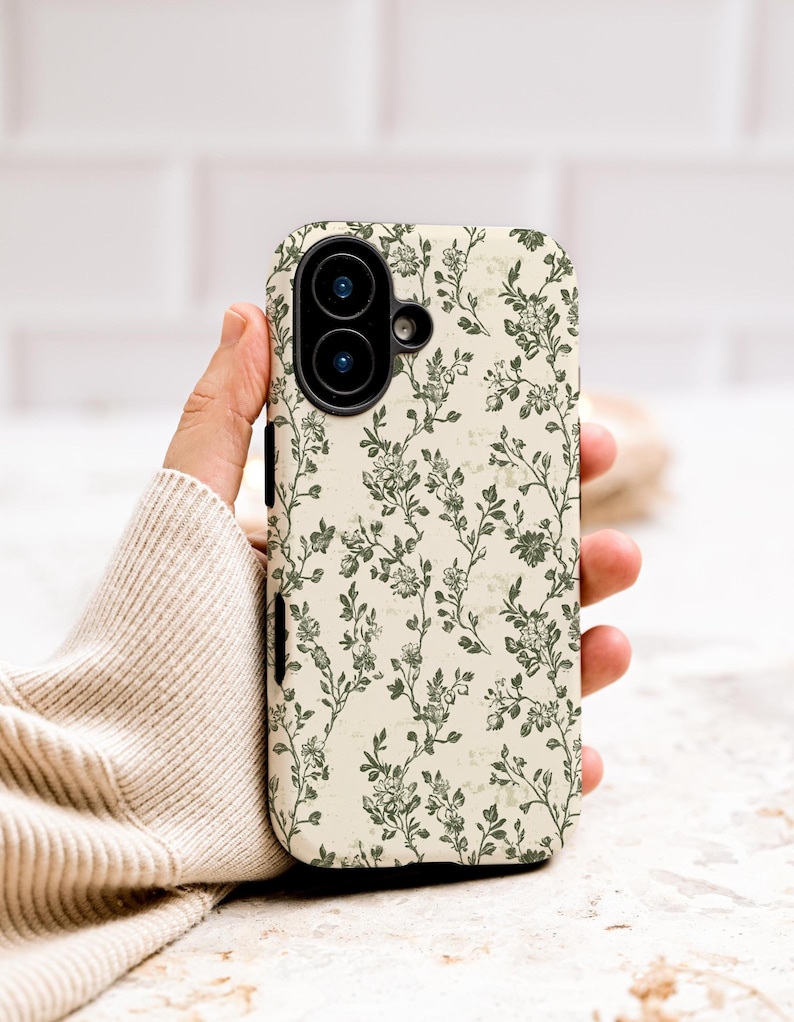 Puede incluir: Una funda de tel&eacute;fono con un estampado floral. La funda presenta un fondo color crema con un dise&ntilde;o repetido de vides y flores florales verdes. La funda del tel&eacute;fono tiene un recorte para la c&aacute;mara.
