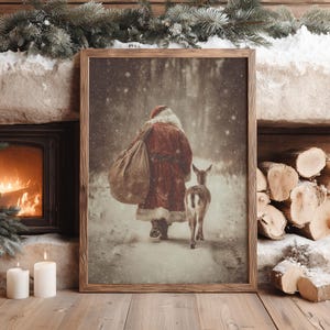 May include: A framed vertical wall art print depicting a figure in a red coat with white fur trim and a matching hat, carrying a large brown sack over one shoulder, walking through a snowy forest alongside a small deer in the falling snow.