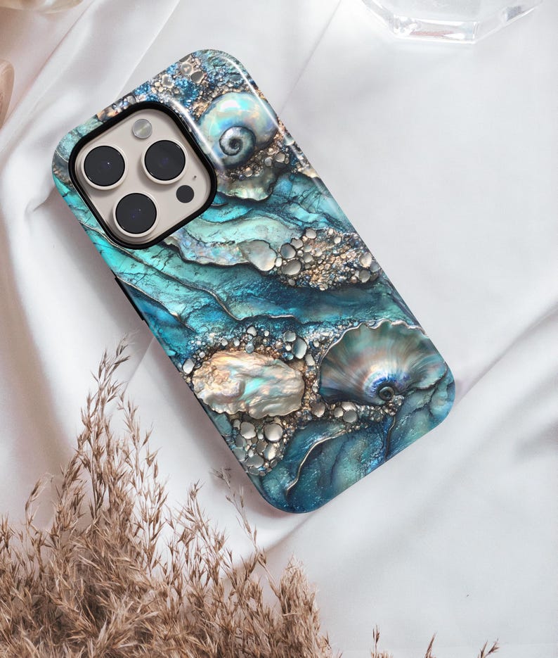 May include: A blue and gold iPhone case with a seashell design. The case has a textured surface and a camera cutout.