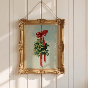 May include: A framed print featuring a sprig of mistletoe tied with a red ribbon. The artwork is set in an ornate gold frame and hangs against a white paneled wall. The painting has a vintage aesthetic.