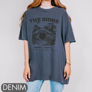 Pode incluir: Uma camiseta azul marinho com um gr&aacute;fico de uma toca de hobbit e o texto "The Shire, Middle-Earth, Second Breakfast, Ale, and Lembas".