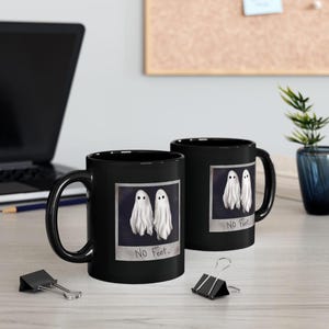 May include: Two black coffee mugs with a white ghost design and the text "No Feet." printed on them.