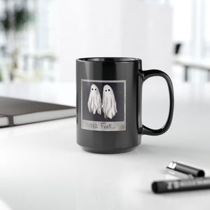 May include: Black coffee mug with a white ghost image and the text "No Feet." printed on it.