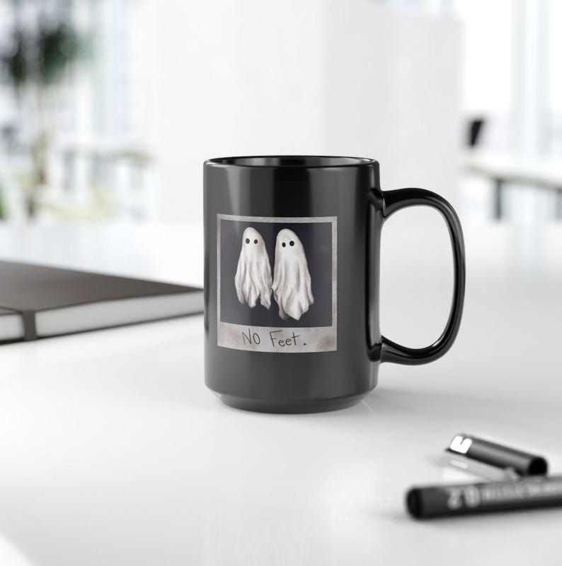 May include: Black coffee mug with a white ghost image and the text "No Feet." printed on it.