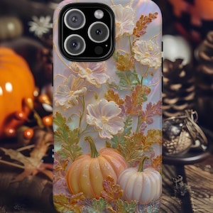 May include: A phone case featuring an iridescent, pearlescent finish with a raised design of two pumpkins and delicate white flowers surrounded by golden-hued foliage. The surface displays a soft, shimmering color palette with light pink and gold tones.