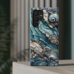 May include: A blue and white phone case with a seashell design. The case has a camera cutout and a textured surface.