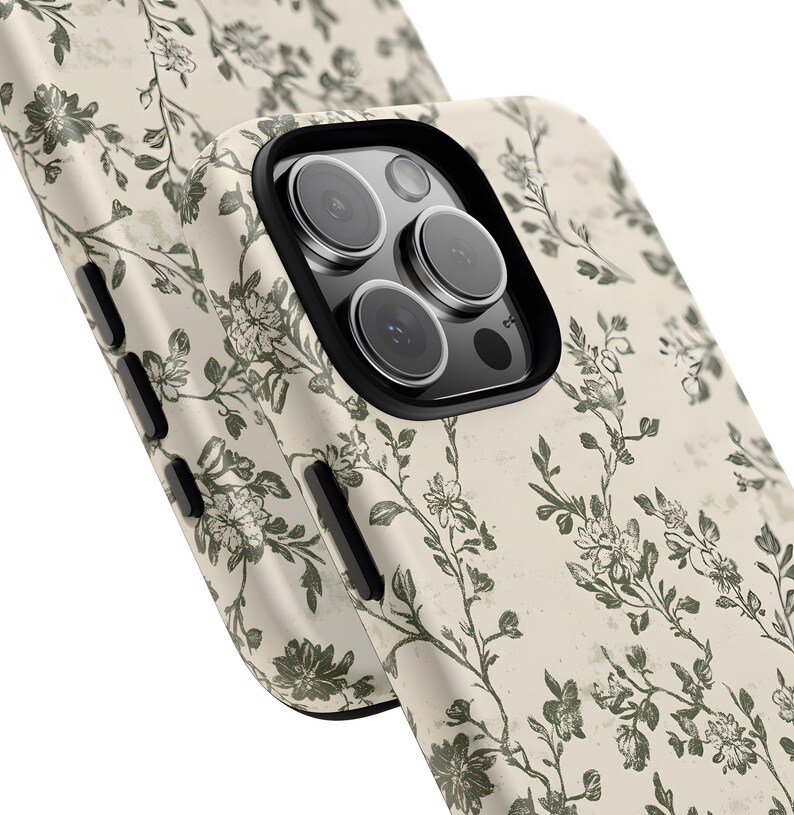 Puede incluir: Primer plano de dos fundas de tel&eacute;fono con un estampado floral. Las fundas son de color blanco roto con un aspecto envejecido y presentan un dise&ntilde;o repetido de flores y enredaderas verdes. La funda del tel&eacute;fono tiene un protector de lente negro.