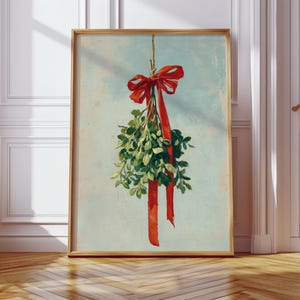 May include: Framed art print featuring a sprig of green mistletoe tied with a red ribbon and bow. The artwork has a vintage aesthetic with a light blue background and a wooden frame. The print is displayed on a wooden floor.
