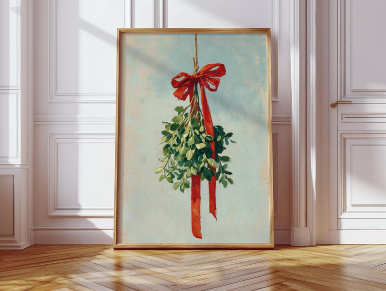 May include: Framed art print featuring a sprig of green mistletoe tied with a red ribbon and bow. The artwork has a vintage aesthetic with a light blue background and a wooden frame. The print is displayed on a wooden floor.