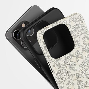 May include: Three phone cases stacked together. The top case is white with a black floral design. The middle case is black, and the bottom case is gray. The cases are angled towards the viewer.