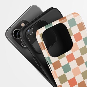 May include: Three smartphone cases. The top case has a retro checkerboard pattern in peach, green, and brown squares. The middle case is black, and the bottom case is gray. The cases are stacked at an angle.