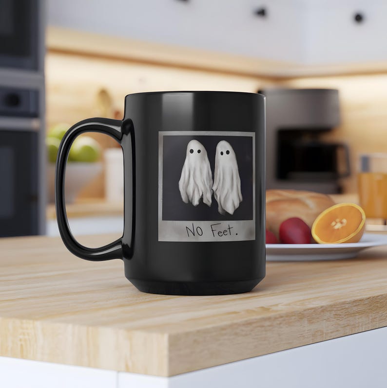 May include: Black coffee mug with a white image of two ghosts with the text "No Feet." printed below the image.