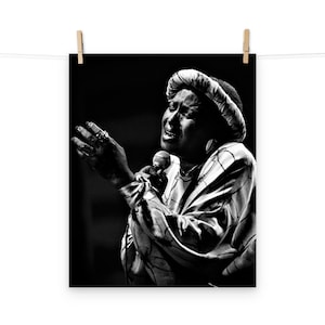 Peut inclure: Photographie en noir et blanc d'une femme chantant dans un microphone. Elle porte un couvre-chef à motifs et une robe à manches longues à motifs.