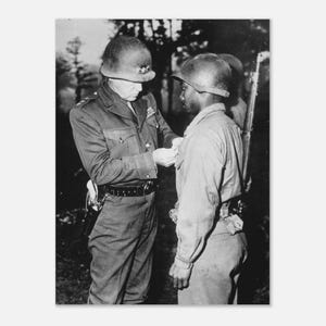 Peut inclure: Photographie en noir et blanc d'un officier militaire épinglant une médaille sur un soldat. Les deux hommes portent des casques et des uniformes. L'officier est en uniforme sombre avec une ceinture et un étui. Le soldat est en uniforme clair.