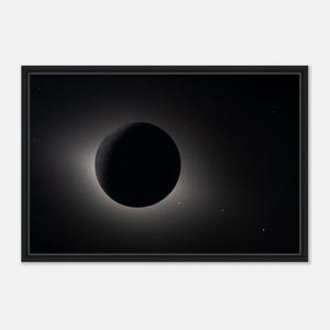 May include: A framed black and white print depicting a celestial event. A large, dark sphere is centered, surrounded by a bright, glowing halo. The background is a deep black, with faint stars scattered throughout.