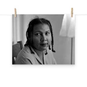 May include: Black and white portrait of a woman with braided hair, wearing a light-colored shirt. She is looking directly at the camera.