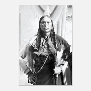 May include: Black and white portrait of a Native American man. He is wearing traditional clothing, including a feathered headdress, a decorated shirt, and a necklace. The man is looking directly at the camera with a serious expression.