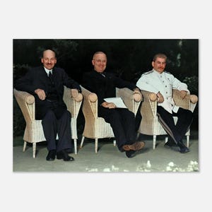 May include: Three individuals seated in light-coloured wicker chairs. The person on the left wears a dark suit and tie. The person in the centre wears a dark suit and glasses, holding papers. The person on the right wears a white military-style uniform.