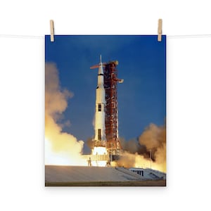 May include: A white and red rocket on a launch pad with smoke and fire coming from the bottom. The rocket is surrounded by a cloudy sky.