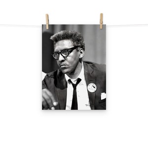 May include: Black and white photograph of a man wearing glasses and a suit with a button that says "We Shall Overcome" on it.