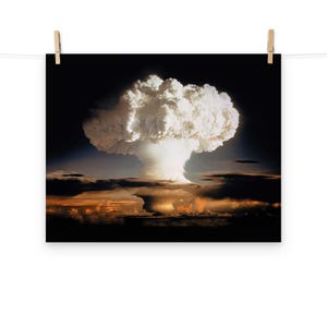 Pode incluir: Uma fotografia a preto e branco de uma nuvem em forma de cogumelo de uma explosão nuclear. A nuvem é grande e branca, com um centro escuro. A nuvem está sobre um céu escuro, com algumas nuvens visíveis à distância.