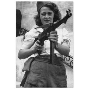 May include: Black and white photograph of a person holding a submachine gun. The person is wearing a white blouse, dark pants, and a hat. A band is visible on the person's arm. The image is a historical portrait.