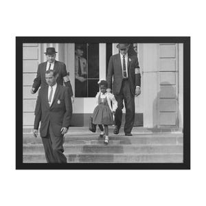 Pode incluir: Uma fotografia a preto e branco de uma menina com um vestido a entrar num edifício escolar, escoltada por dois homens de fato. A menina leva uma pequena mala. A fotografia está enquadrada numa moldura preta.