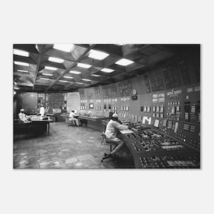 Könnte beinhalten: Ein Schwarz-Weiß-Foto eines großen industriellen Kontrollraums mit einer geschwungenen Konsole, die zahlreiche Knöpfe, Schalter und Anzeigen aufweist. Drei Personen sitzen an Arbeitsplätzen unter einer geometrischen Kassettendecke.