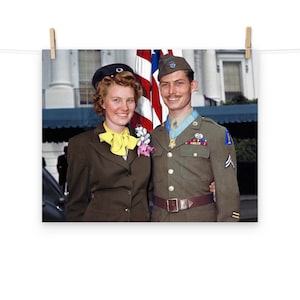 May include: A couple poses for a photo in front of an American flag. The man is wearing a military uniform with medals and a hat. The woman is wearing a brown suit with a yellow bow and a flower pin.