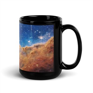 May include: Black coffee mug with a colorful nebula image. The image shows a swirling cloud of gas and dust with bright stars.